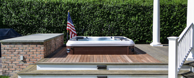 Hot Tub with American flag standing beside it; hot tub is sent into a deck and behind very tall hedges act as privacy shield
